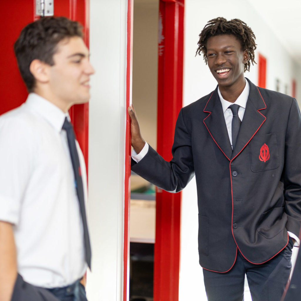 Two senior male students in school uniform stand by door laughing